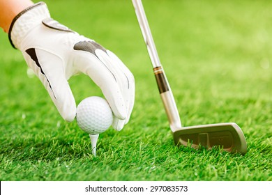 Hand putting golf ball on tee with club in golf course - Powered by Shutterstock