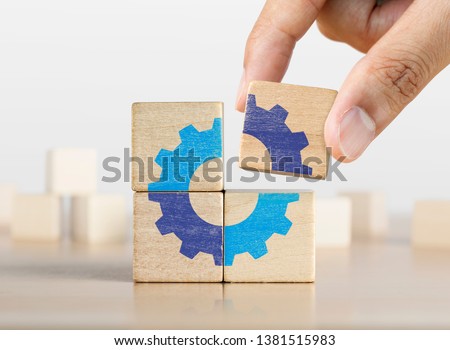 Hand putting the last piece of wooden blocks with the gear icon. Team work, unity, partnership or integration concept.