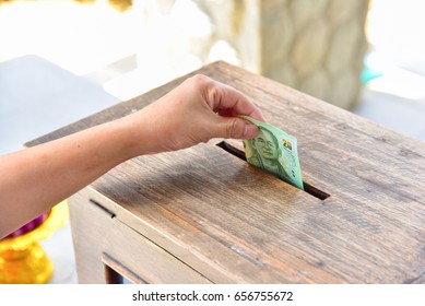 Hand Putting Money Into A Wooden Donation Box