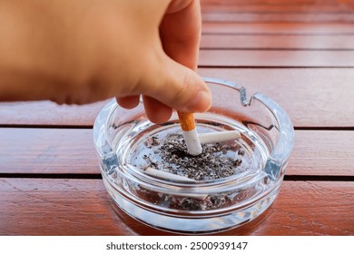 Hand putting out cigarette in ashtray. Glass ashtray with cigarette butts, Ash and cigarettes. Health concept.