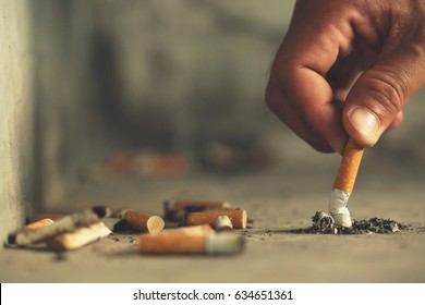 Main mettant une cigarette, mégot sur le sol en Béton, ciment nu.