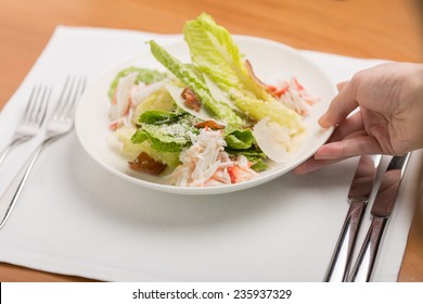 Hand Putting Plate Of Crab Salad On Wooden Table