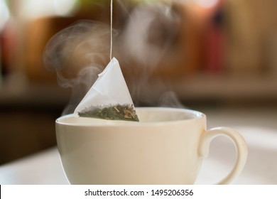 Hand Putting A Pyramid Tea Bag In A Hot Water Cup In The Morning