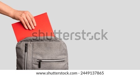 Hand putting red book, textbook into backpack, school bag. Banner background.