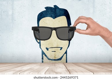 Hand putting sunglasses on wall drawing face - Powered by Shutterstock