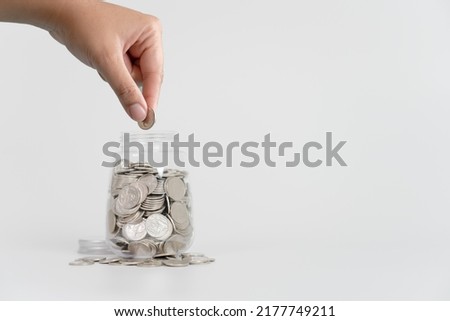 Hand putting Thai currency coin in saving jar