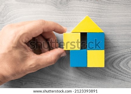 Hand putting together a house made of blocks