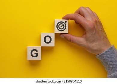 Hand putting wooden blocks with letters go and a target icons on yellow background. Business development strategy, advancement and goal concept.