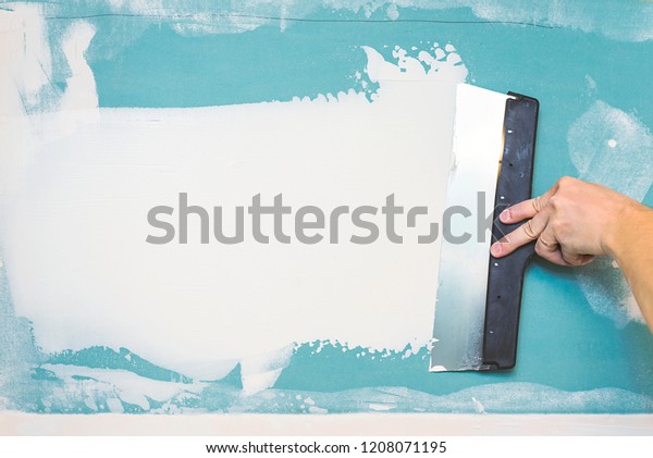 Hand with putty knife repair\
wall, Hand with a spatula, spatula with spackle paste structure,\
process of applying layer of putty trowel, working with spackling\
paste