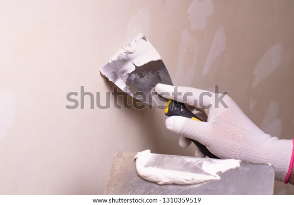 Hand with putty knife repair\
wall, Hand with a spatula, spatula with spackle paste structure,\
process of applying layer of putty trowel, working with spackling\
paste