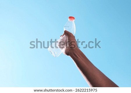 A hand raises an empty plastic bottle against a clear blue sky, symbolizing hope and a call for environmental awareness. This image represents the importance of recycling, reducing plastic waste