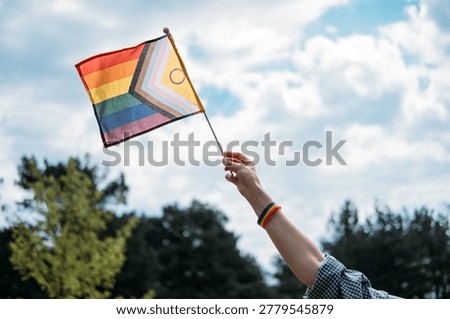 Hand raises progress pride flag against cloudy sky. Human rights advocacy, social justice movement, LGBTQ equality protest.