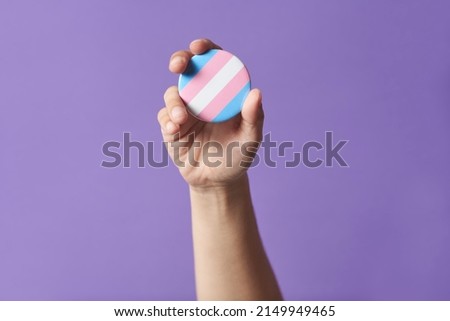 Hand raising a trans flag badge or pin on a purple background. Concepts of identity pride, gender diversity visibility, equality and non discrimination. Foto stock © 