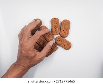 Hand reaches down to select one of several brown rectangular biscuits arranged randomly on a clean white surface suggesting a simple snack break or craving moment.