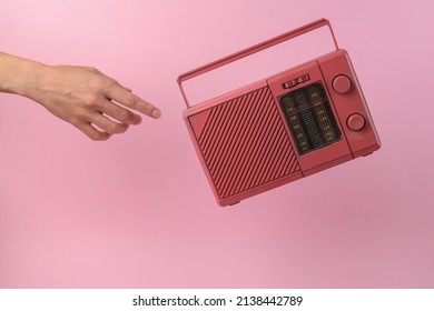 Hand reaches for levitating retro fm radio receiver on pink background - Shutterstock ID 2138442789