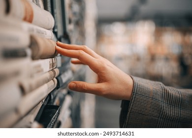 A hand reaches out to touch the spine of a book in a bookshelf, the rest of the bookstore is blurred out in the background.