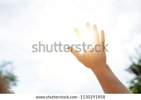 a hand reaches for the sky and covers the sun, the sun's rays make their way through the hand, close - up