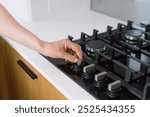 A hand is reaching to adjust the burner knob on a sleek gas stove. Close up shot of a woman turn on flame on cooker hob in a stylish kitchen. Person ready for cooking at home