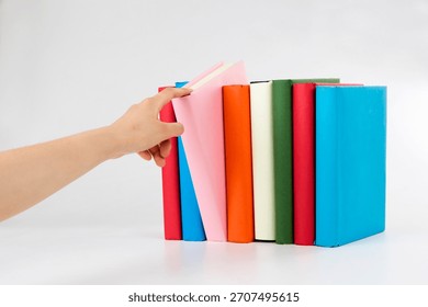 Hand reaching for a book in a colorful array of neatly arranged hardcover books in a minimalist setting