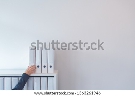 Hand reaching for document ring binder on office shelf, businesswoman taking file folder with documentation, plenty of blank white copy space