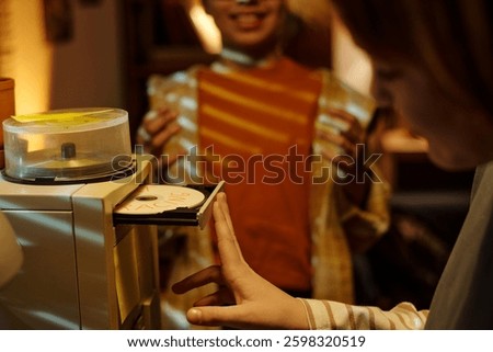 Hand reaching for a DVD from a spindle while person in background looks on with a smile, both expressing contentment during a storage operation