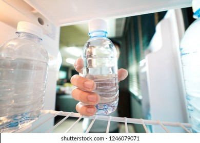 Hand Reaching Into Refrigerator Taking A Plastic Bottle Of Water Out. Wide Angle Perspective.