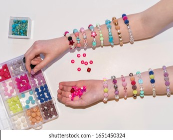 Hand reaching into a tray of colorful beads during a craft project to make many bracelets - arms covered in rows of bracelets recently made
