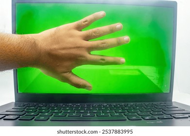 A hand reaching out from a laptop screen with a green background, creating an illusion of interaction. Perfect for technology, virtual reality, or augmented reality concepts - Powered by Shutterstock