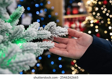 A hand reaching out to a snowy tree branch amidst festive lights. Background filled with colorful bokeh lights creating a cozy atmosphere - Powered by Shutterstock