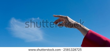 Hand is reaching up towards a cloud in the sky. Concept of wonder and curiosity, as if the hand is trying to grasp the cloud and bring it closer. The blue sky and the cloud create a serene