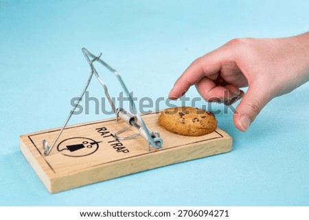 Hand reaching towards a cookie placed on a rat trap in a playful setting