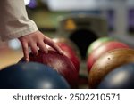 Hand reaching for vibrant bowling ball in colorful, well-lit bowling alley with various balls and blurred background creating dynamic atmosphere