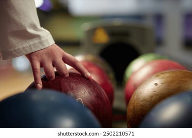 Hand reaching for vibrant bowling ball in colorful, well-lit bowling alley with various balls and blurred background creating dynamic atmosphere