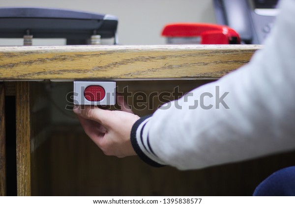 A hand ready to press a panic button under an\
administrative desk