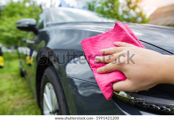 A hand with\
a red rag wipes water drops on a car after washing with car shampoo\
and wax in the country. Hand\
wash