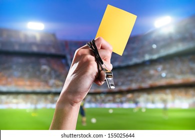 Hand Of Referee With Yellow Card And Whistle In The Soccer Stadium.