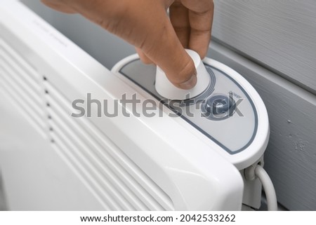 Hand regulating, setting temperature on electric convector, heater thermostate in the room in winter, climate control and energy saving concept
