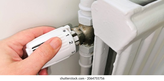 Hand regulating thermostat on district heating radiator - Shutterstock ID 2064755756