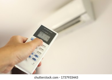 Hand with remote control directed on air conditioner inside the room