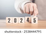 Hand replaces "2024" with "2025" using number blocks, symbolizing the transition into the new year, representing change, progress, and the ongoing passage of time