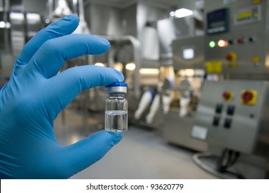 Hand in rubber glove holding a bottle of medicine against the background of the production line drugs