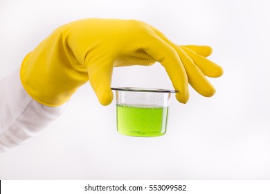 Hand With Rubber Glove Holding Dosage Cup With Green Detergent Against White Background. Safety Cleaning Products Usage Indoor