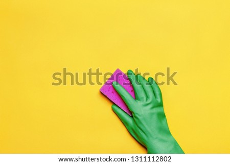 A hand in a rubber protective glove with a pink sponge on a yellow background. Cleaning concept.