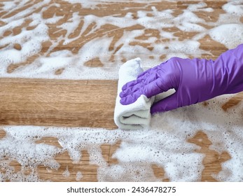 A hand in a rubber purple glove wipes the floor with soap foam with a white rag - Powered by Shutterstock