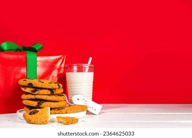 Hand of Santa Claus with traditional Christmas cookie snack with milk glass. Santa Dunking Cookie, on bright festive red and white wooden  background. Merry Christmas and Happy New Year greeting card - Shutterstock ID 2364625033