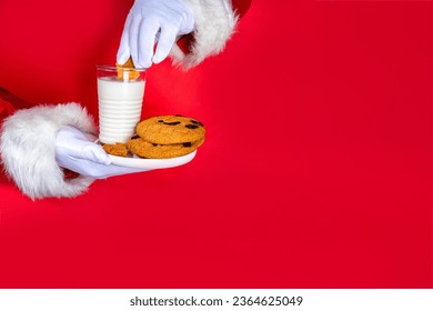 Hand of Santa Claus with traditional Christmas cookie snack with milk glass. Santa Dunking Cookie, on bright festive red torn paper hole background. Merry Christmas and Happy New Year greeting card - Shutterstock ID 2364625049