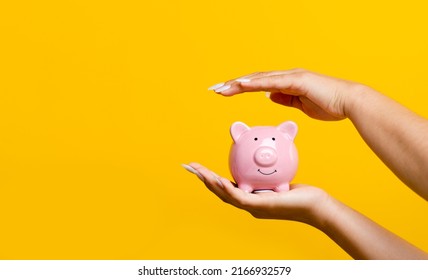 Hand savings and a pink piggy bank with coins inside. enhancing savings The concept of planting a money saving plan and saving expenses increases more income. - Shutterstock ID 2166932579