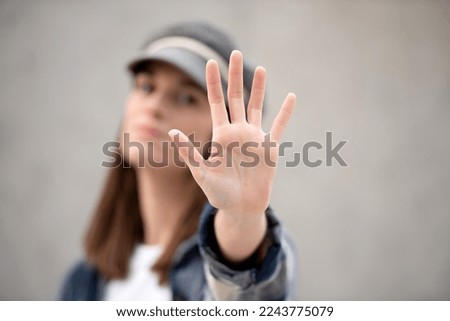 hand saying stop in foreground, in background out of focus girl in cap with serious face