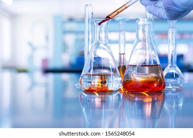 hand of scientist drop orange solution in glass flask in chemistry science laboratory blue background 