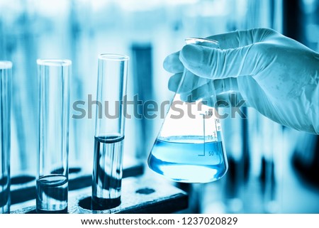 hand of scientist holding flask with lab glassware in chemical laboratory background, science laboratory research and development concept